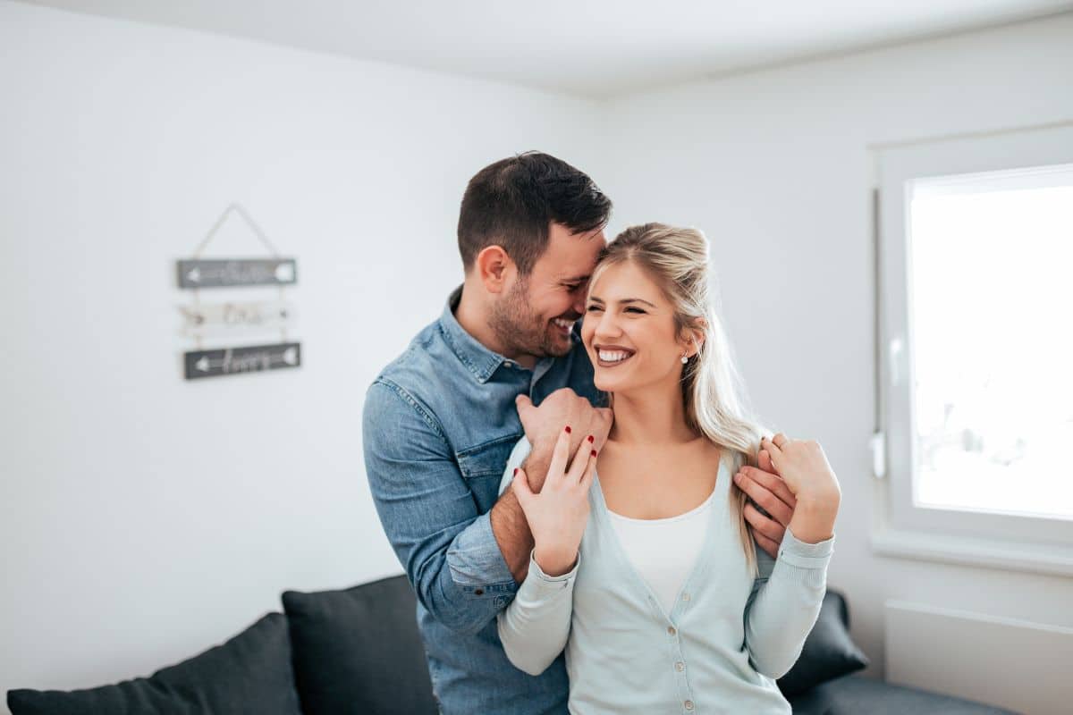 Un couple souriant se tient dans les bras l'un de l'autre dans un salon.