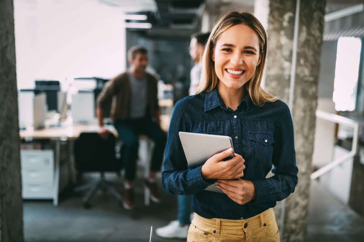 Une femme souriante tient une tablette dans un bureau.