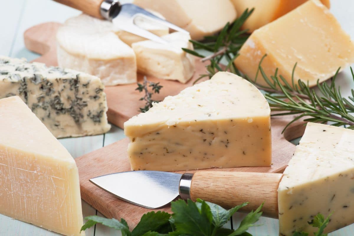 Différents types de fromages sur une planche en bois avec des herbes.