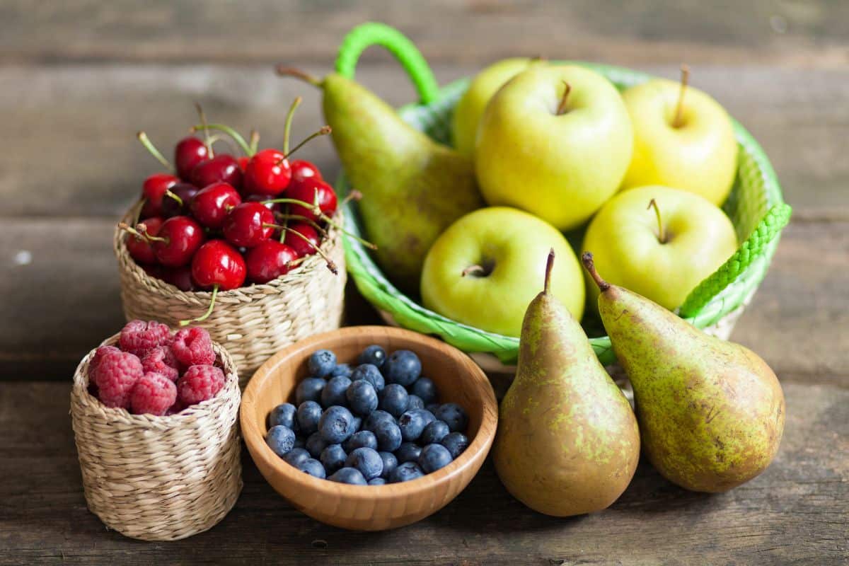 Divers fruits frais disposés dans des paniers en osier et une assiette en bois.