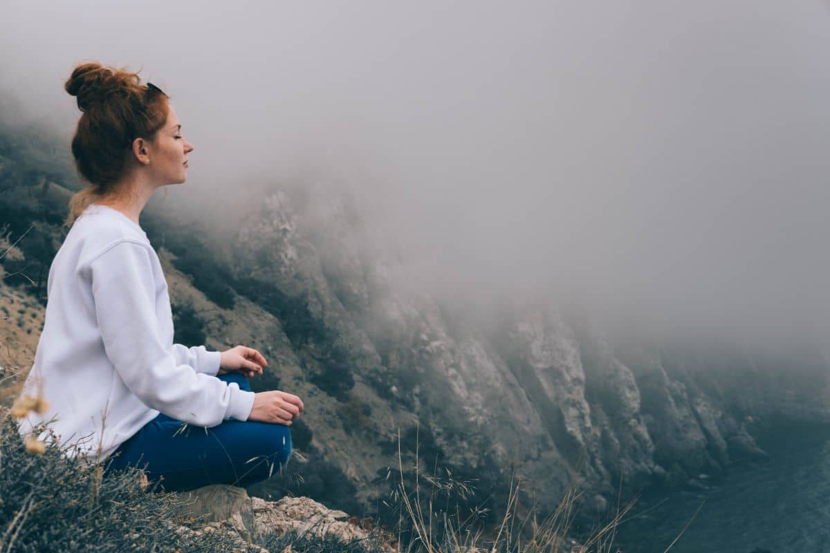 Une femme médite au sommet d'une montagne dans la brume.