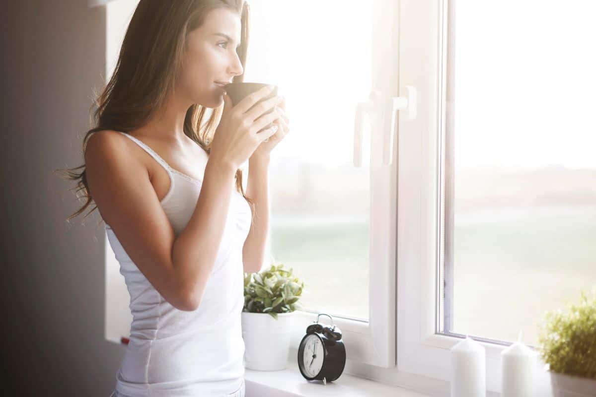 Femme buvant une boisson chaude près d'une fenêtre ensoleillée