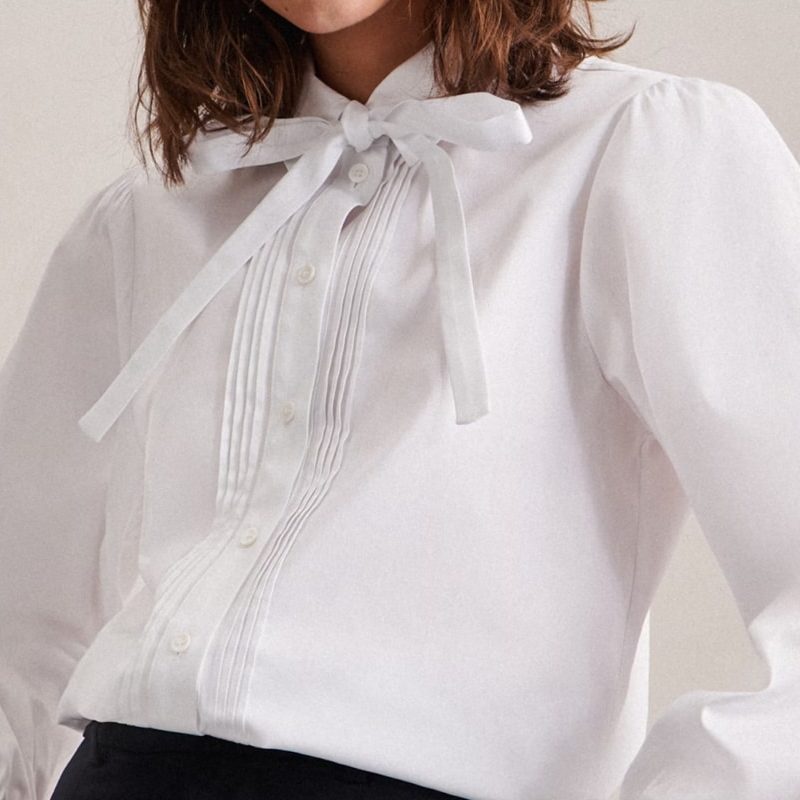 Une blouse blanche avec un col lavallière noué et des détails de plissage.